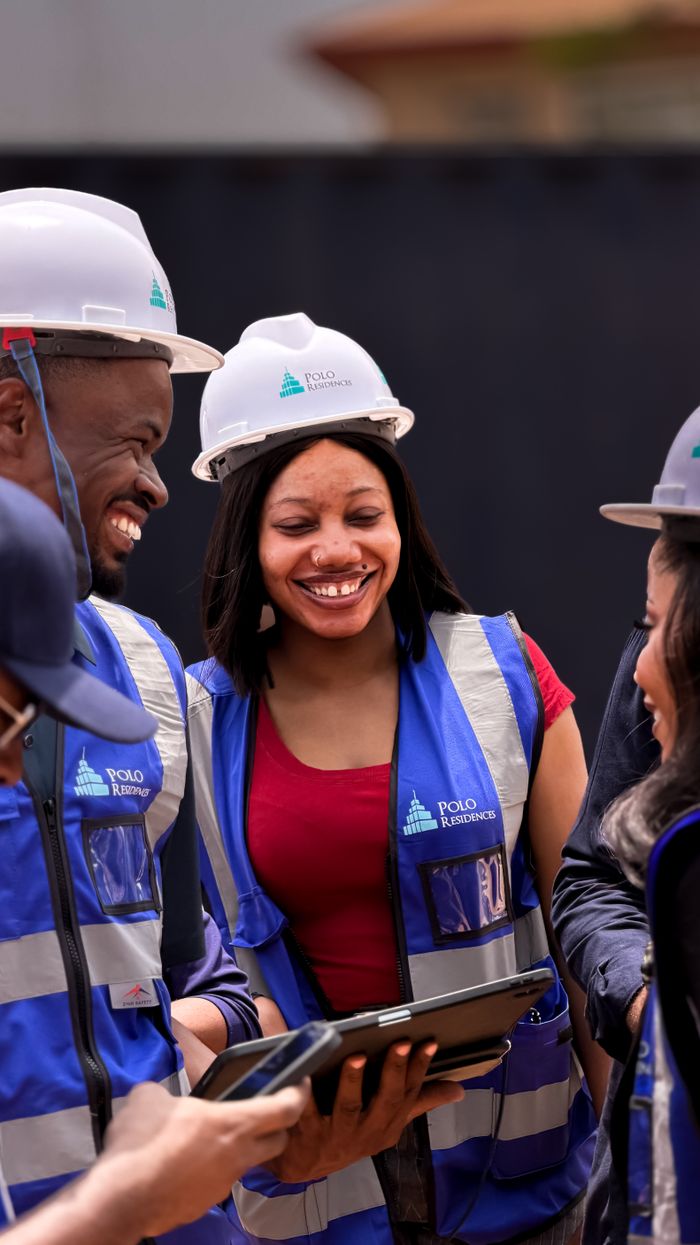 Services A group of construction workers collaborating and smiling outdoors, wearing safety gear and using a tablet.