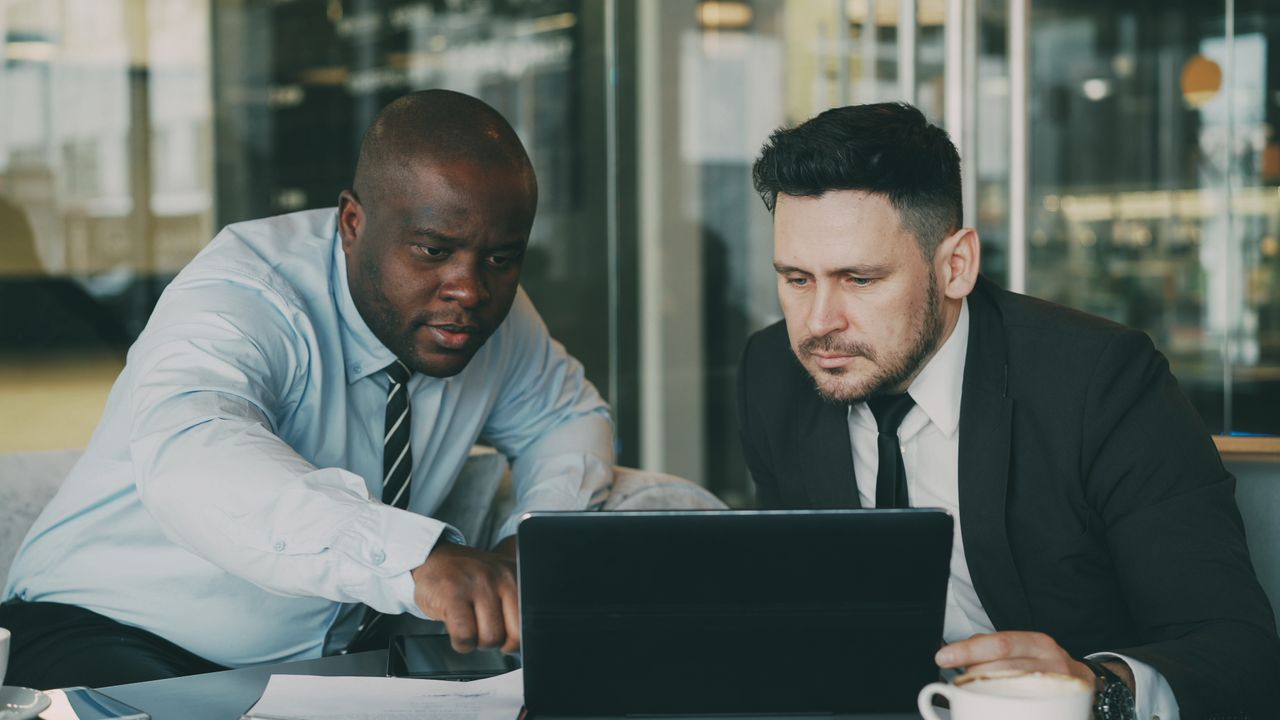 Crafting Captivating Headlines: Your awesome post title goes here Two businessmen concentrating on a tablet, collaborating in a modern office setting.