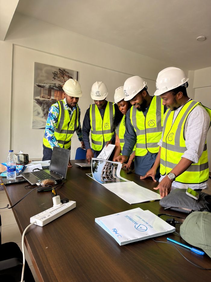 Accueil A group of engineers in safety gear examines architectural plans in an office.