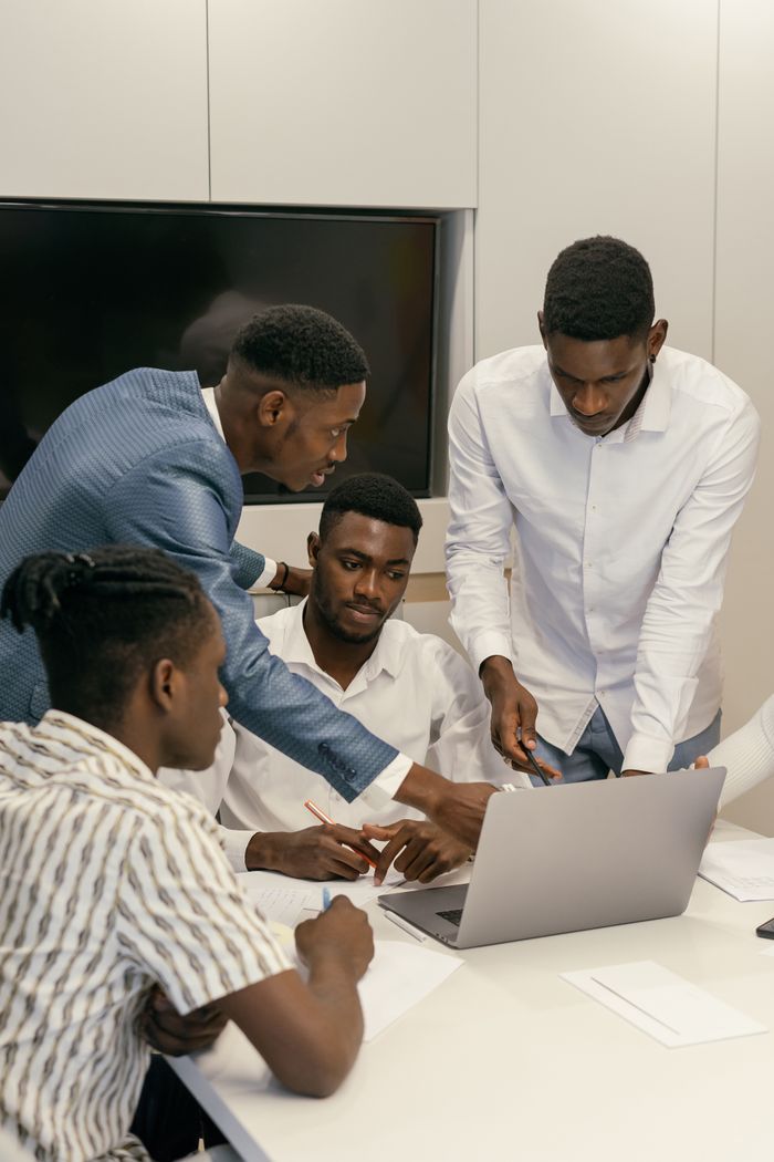 Accueil Four men collaborate on a project using a laptop in a modern office environment.